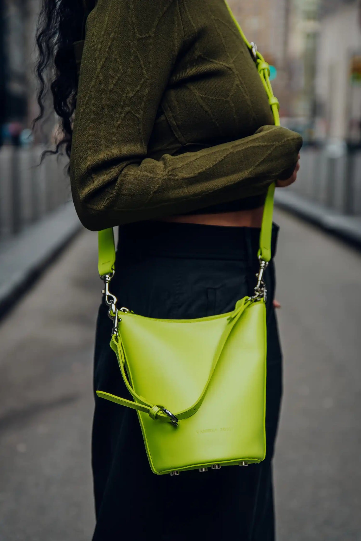 Person holding a bright green handbag on a blurred street background